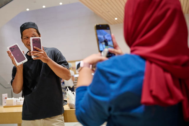 Using their iPhone, a person takes a photo of a customer holding up two iPhone 18 Pro boxes at Apple The Exchange TRX.