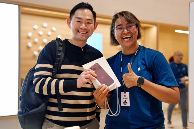 A customer and team member smile and hold iPhone 18 Pro at Apple The Exchange TRX.