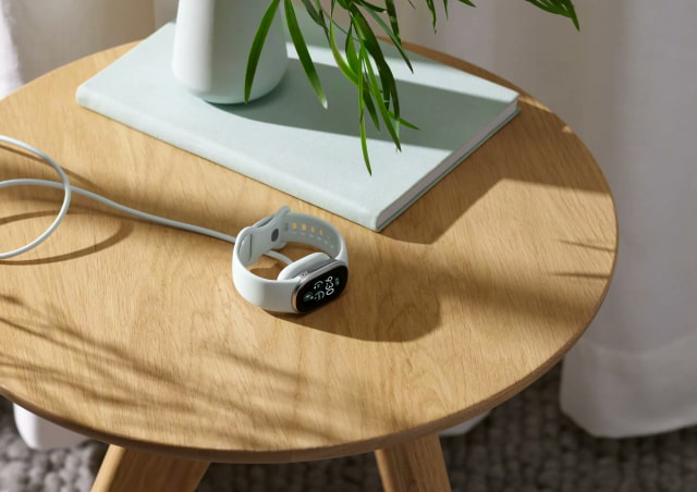 Fitbit Edge connected to its magnetic charging cable on a side table