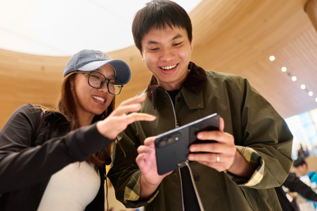 Two customers try an unfolded iPhone Duo in night sky at Apple Jing'an.